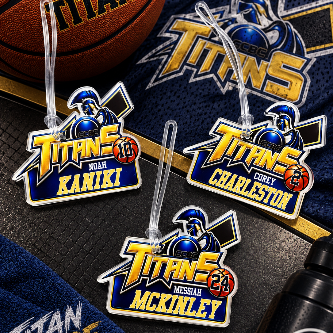 Three custom metal Titans road nameplates with clear plastic hangers, displayed on a dark textured surface with a basketball, navy blue jersey, and a water bottle.